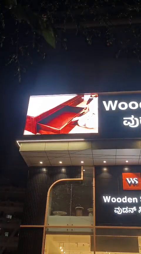 LED display board above a furniture showroom storefront at night, running product visuals