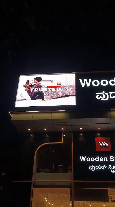 LED display board above a furniture showroom storefront at night, running product visuals