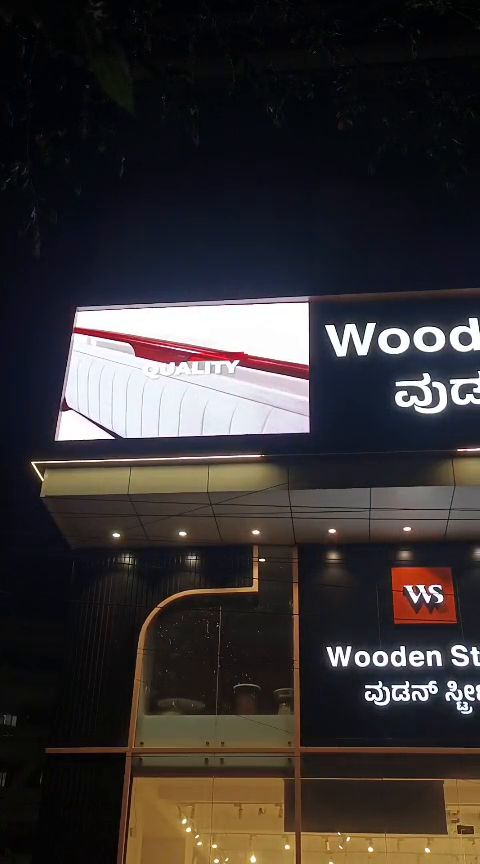 LED display board above a furniture showroom storefront at night, running product visuals