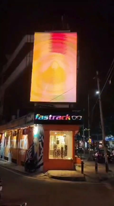 Tall vertical LED display above a corner retail block at night