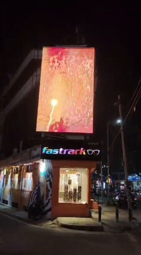 Tall vertical LED display above a corner retail block at night