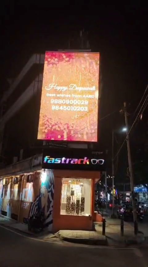 Tall vertical LED display above a corner retail block at night