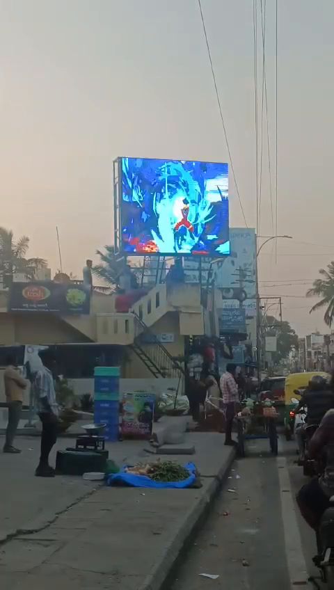 Rooftop outdoor LED screen above a busy street market at dusk